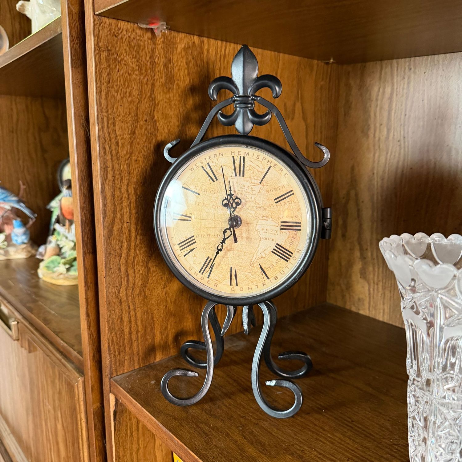 Battery-operated clock with face on each side, scrolled legs and fleur-de-lis top, hairline crack on one clock face, 14"H
