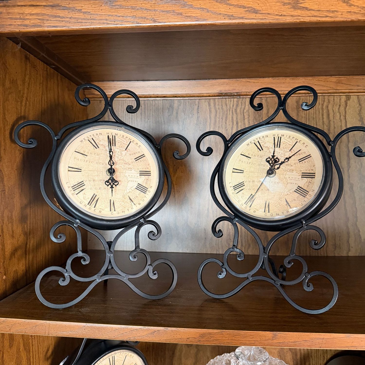 Pair of battery-operated clocks with scrolled metal stands, each plastic face has a hairline crack, 15"H