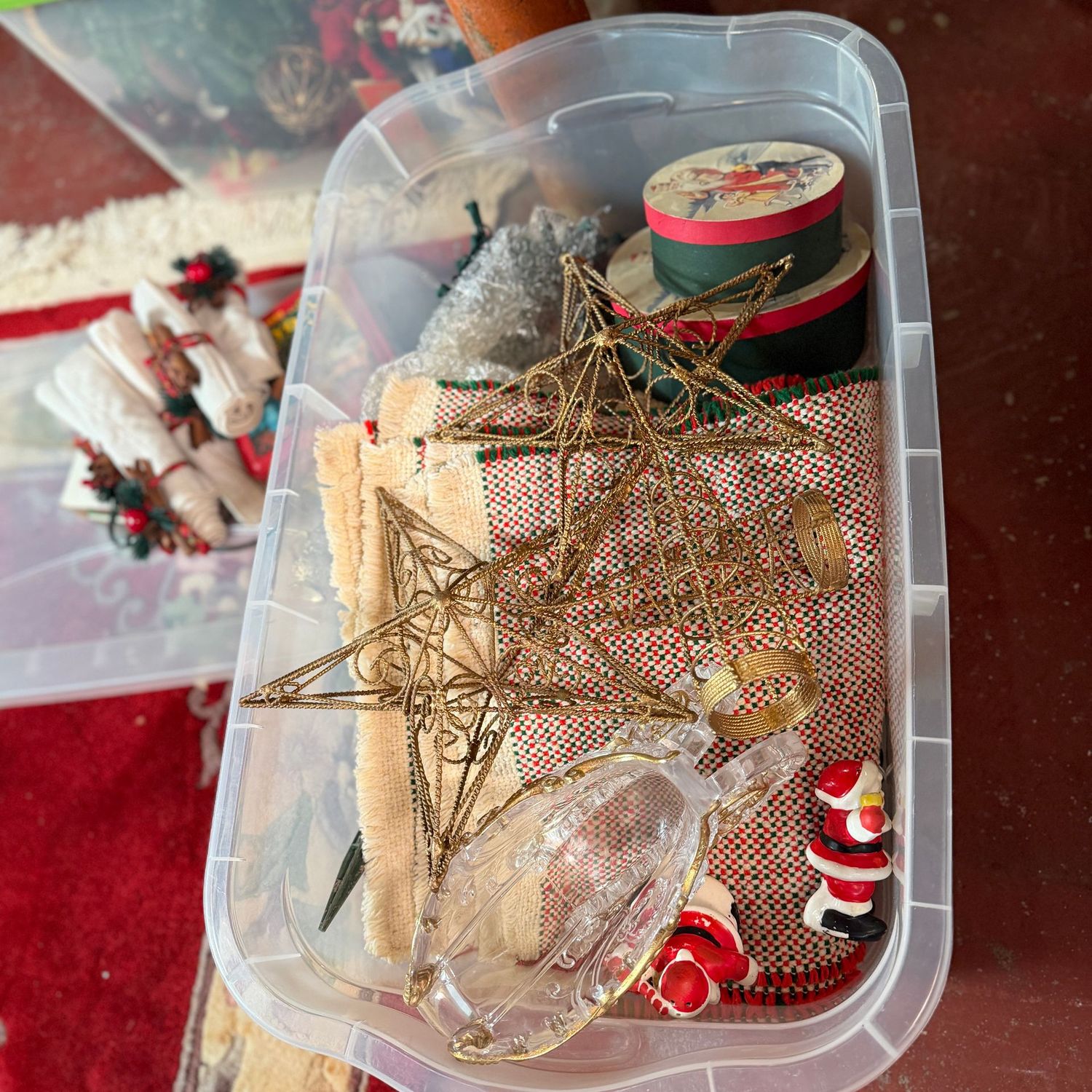Clear bin with lid of Christmas lights, plastic sleigh, placemats, napkins & more
