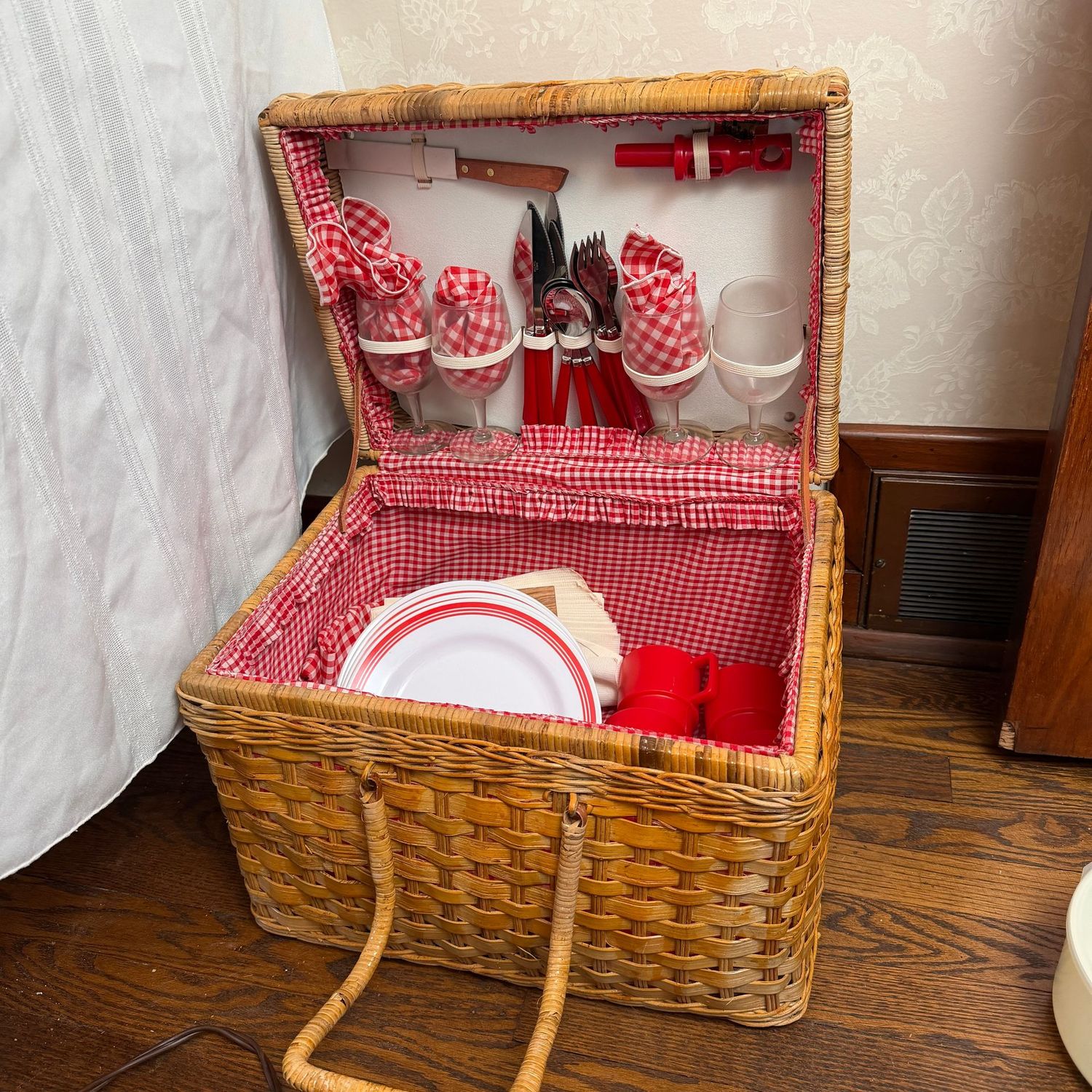 Vintage Picnic Time basket with plastic dishes, silverware, thermos, and red checkered lining, basket shows mild wear, 13"H x 16"W