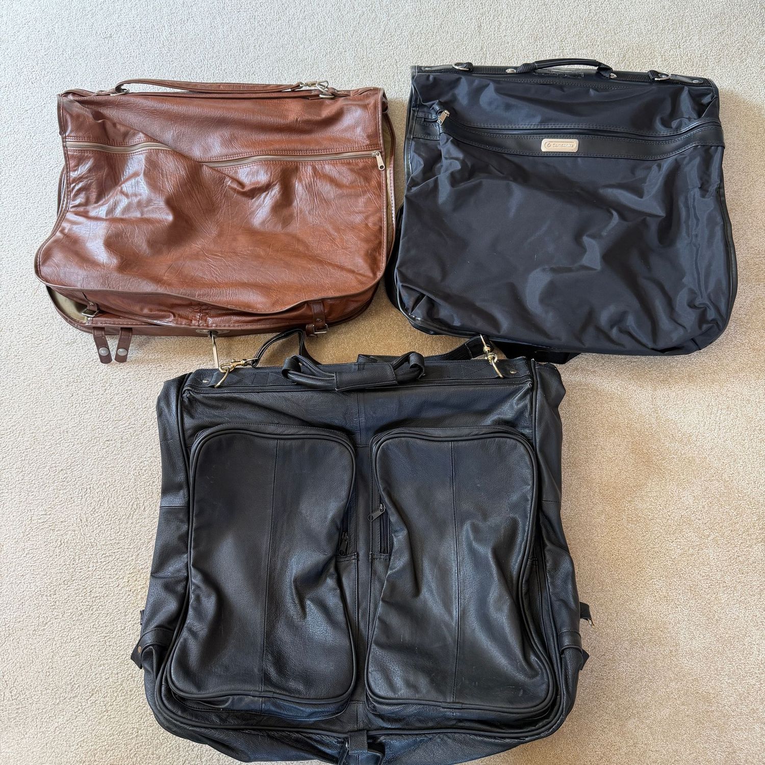 Three garment bags, two are vinyl, one may be leather