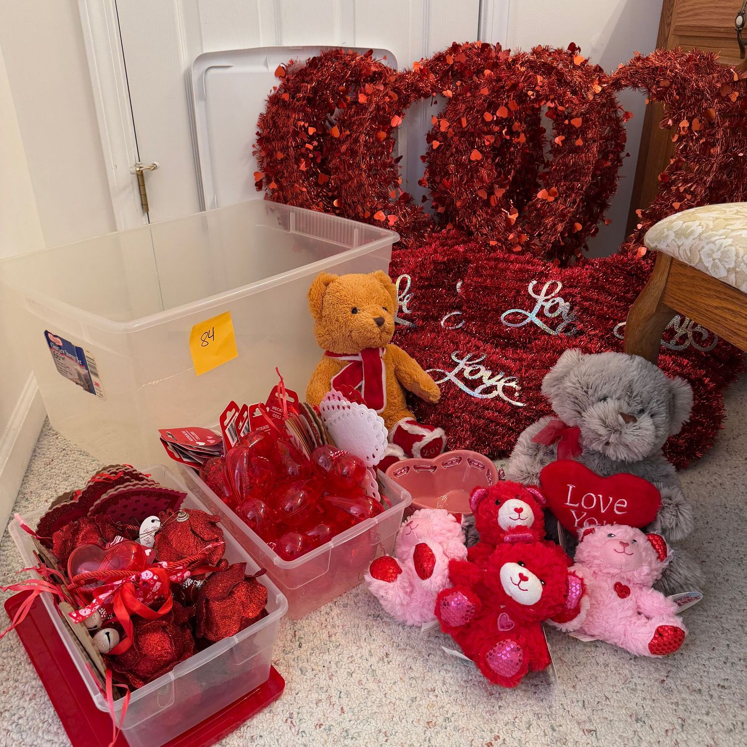Lot #84 large clear bin with Valentine's Day decorations, red rose ornaments, plastic heart ornaments, beads, pressed paper hearts, bears, shimmer heart wall decorations, the largest are 22"H