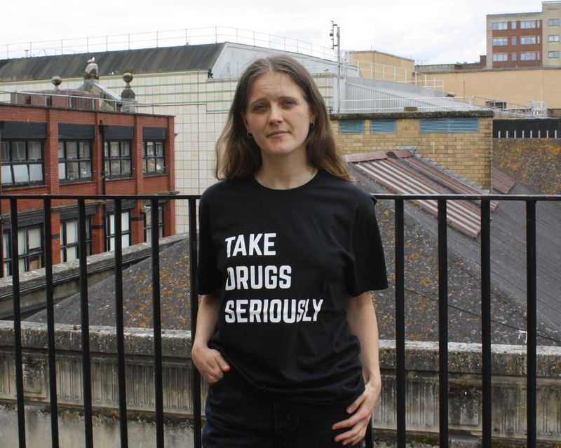 Ester is wearing a short-sleeved black t-shirt with ‘Take drugs seriously’ printed in white across the front.