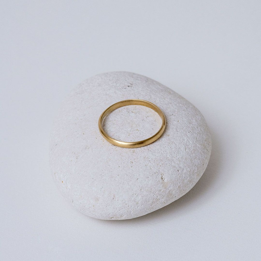 Alliance demi-jonc en or jaune 18K, présentée sur un galet blanc.