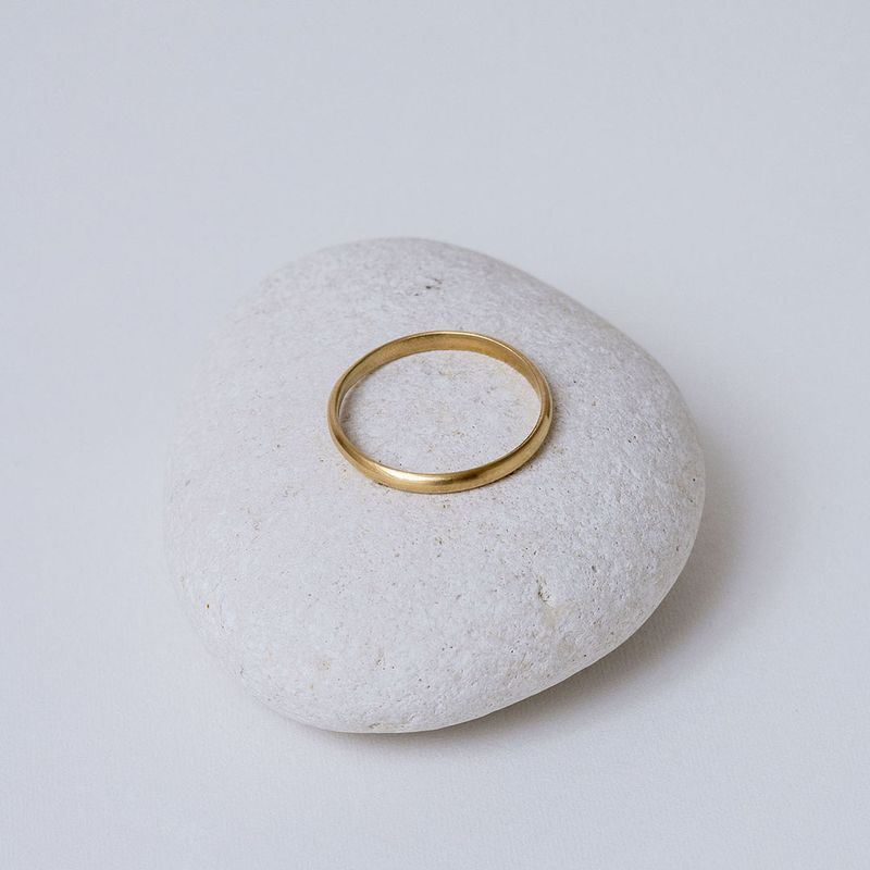 Alliance demi-jonc en or jaune 18 carats, largeur 2 mm, présentée sur un galet blanc.