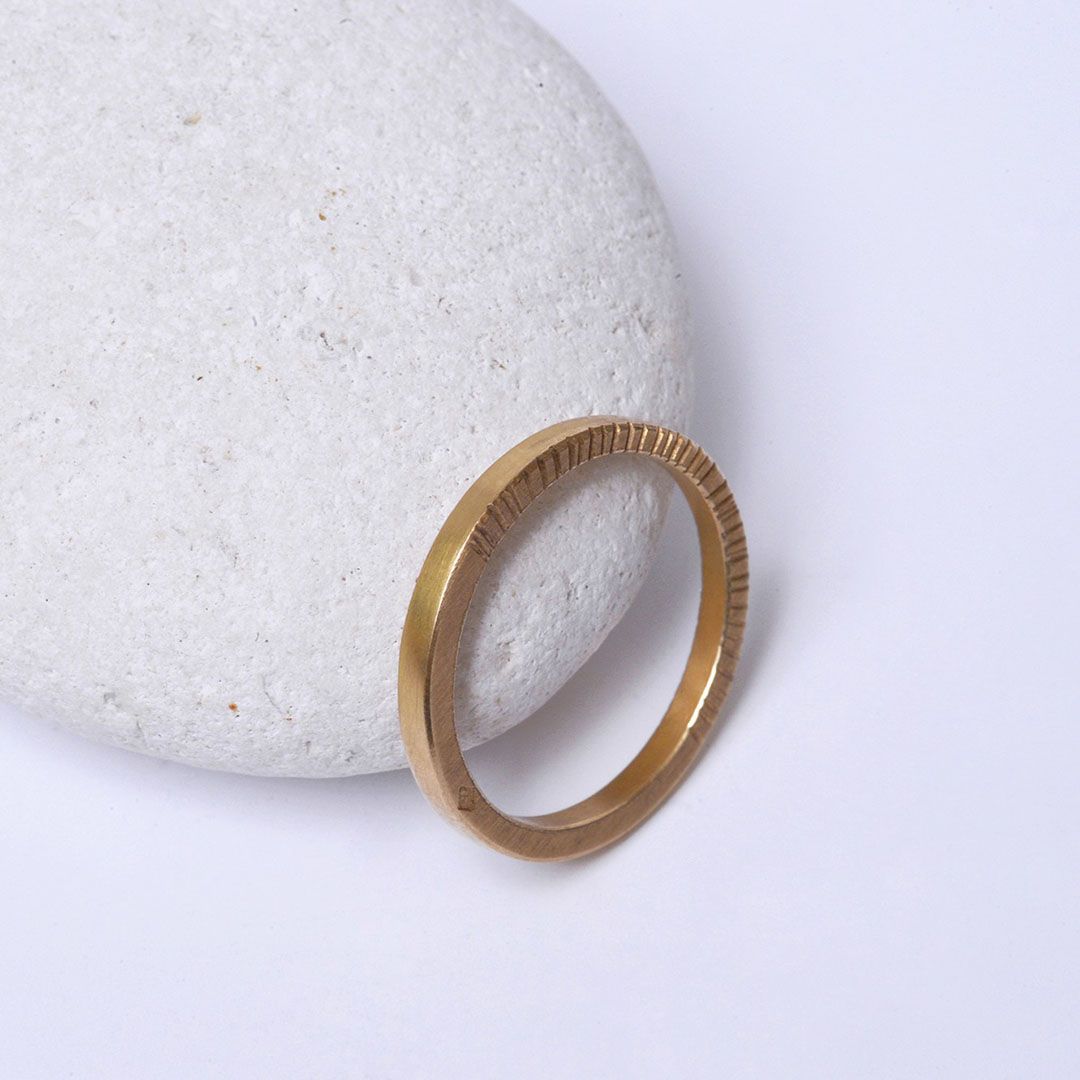 Alliance 2 mm en or jaune 18K, striée présentée contre un galet blanc.