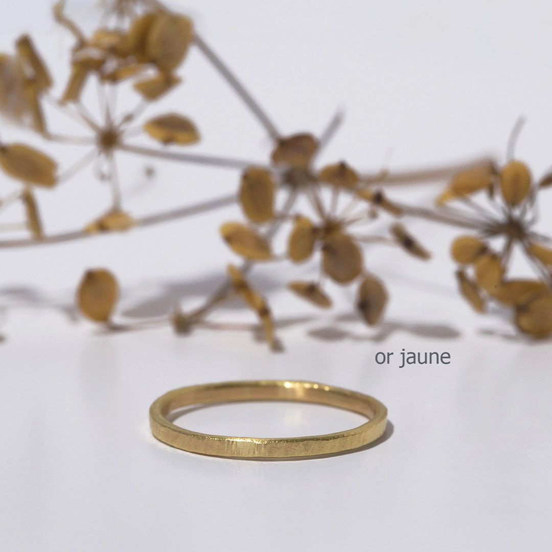alliance fine martelée en or jaune posée devant fleurs séchées. Alliance martelée en or, inspiration nature et authenticité.