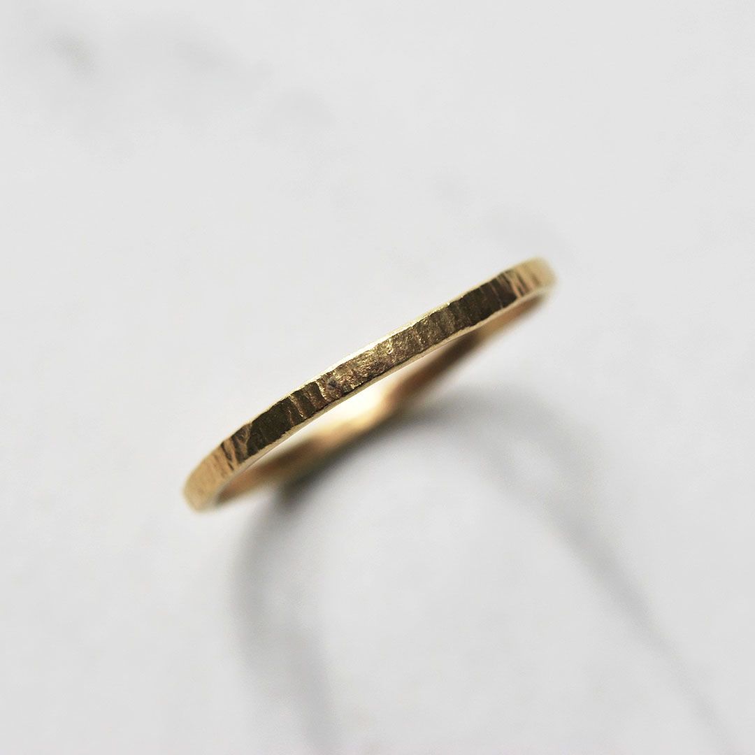 Alliance fine en or jaune sur fond clair. Alliance fine en or jaune, finition martelée raffinée.