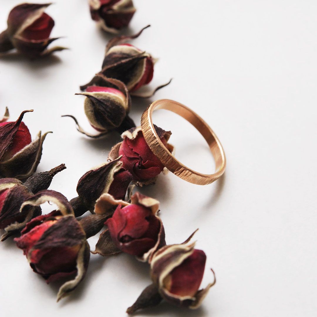 Alliance martelée en or rose 18K, largeur 2 mm, présentée sur roses sechées.