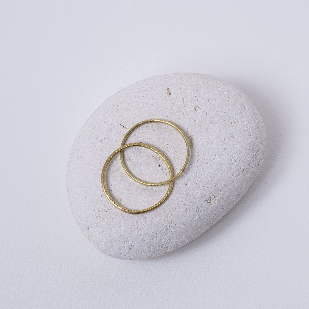 Alliance artisanale en or jaune 18K, deux anneaux fins martelés, présentée sur un galet avec éclats dorés.