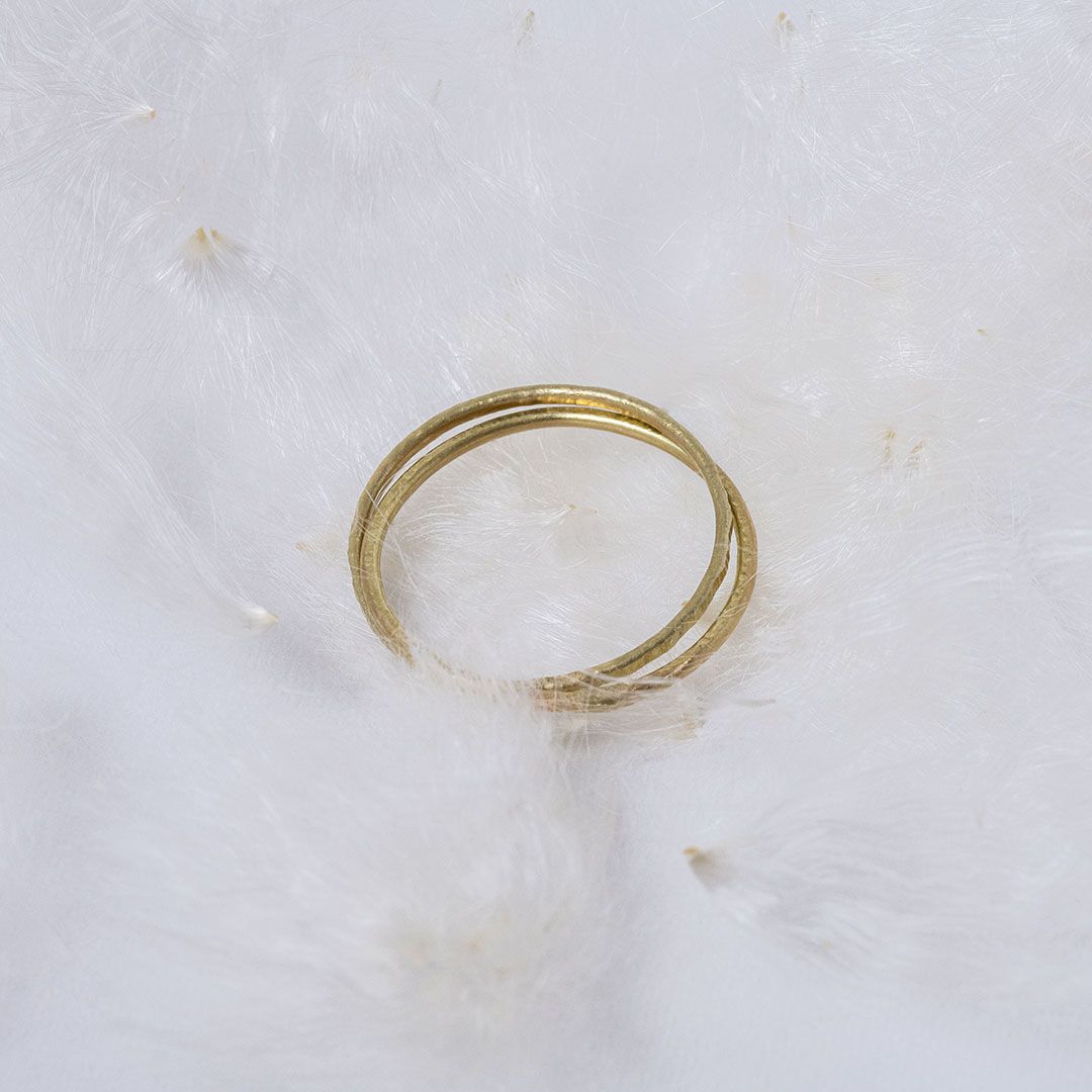 Bague mariage minimaliste en or 18K, deux anneaux martelés, sur fond de plumes blanches. 