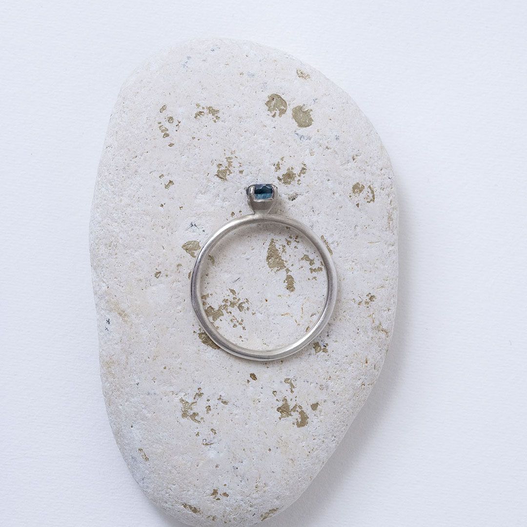 Bague en argent avec topaze bleue, présentée sur un galet aux éclats dorés.