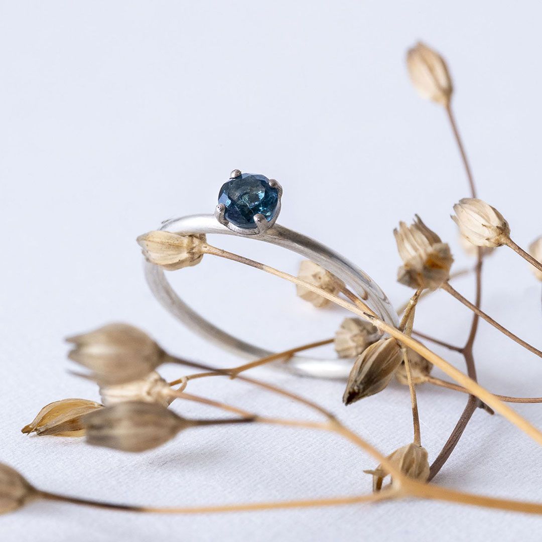 Bague en argent avec topaze bleue, posée sur une branche de végétaux.