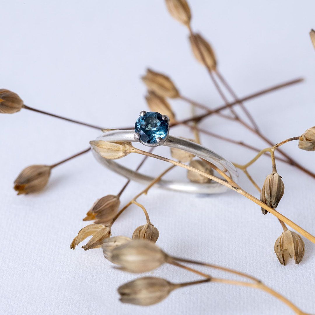 Bague en argent avec topaze bleue, posée sur une branche de végétaux.