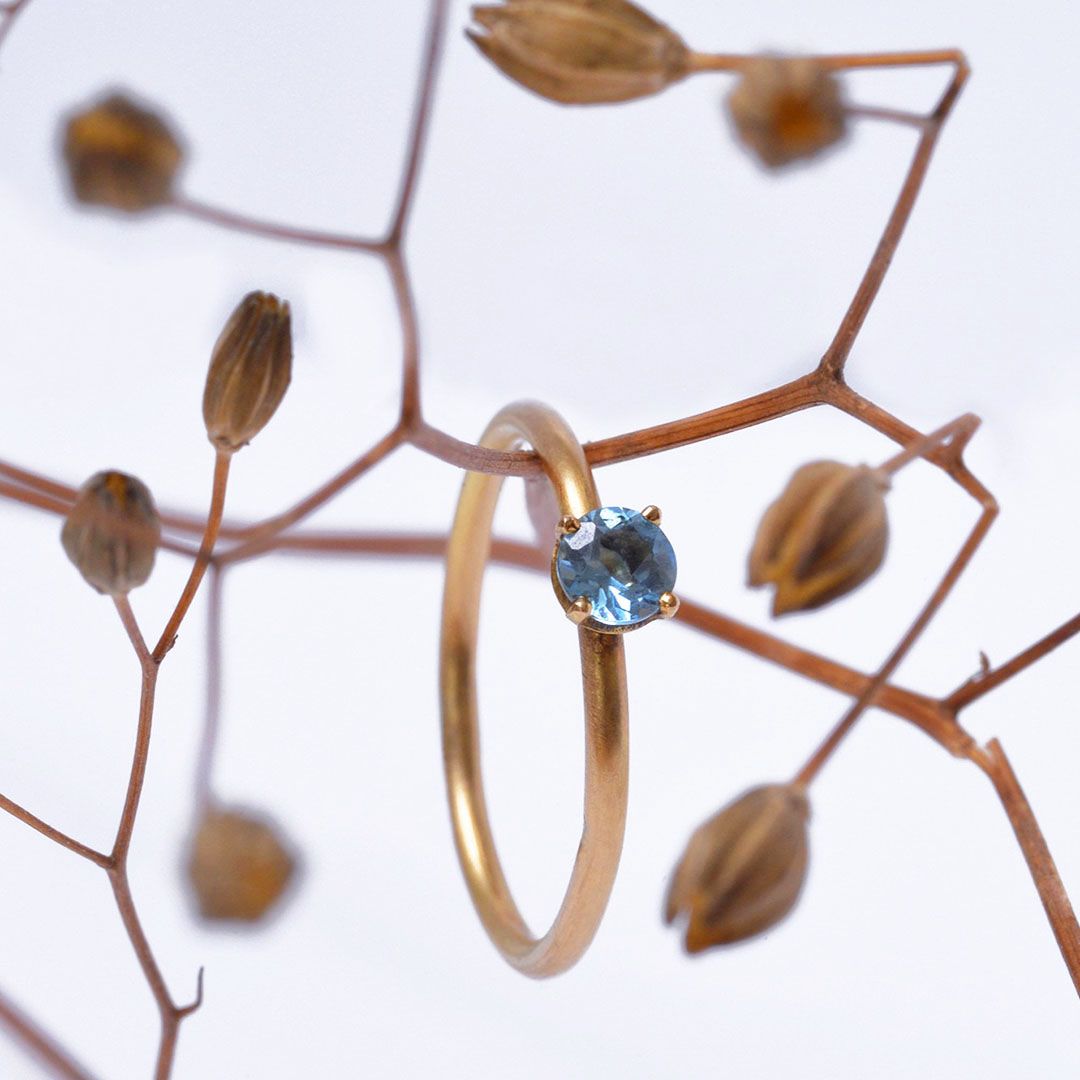 Bague en or jaune et topaze bleue, bague de demande en mariage. présentée sur une branche de végétaux.