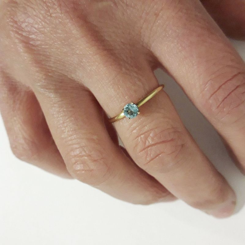 Bague de fiançailles en or jaune 18K avec topaze bleue portée au doigt