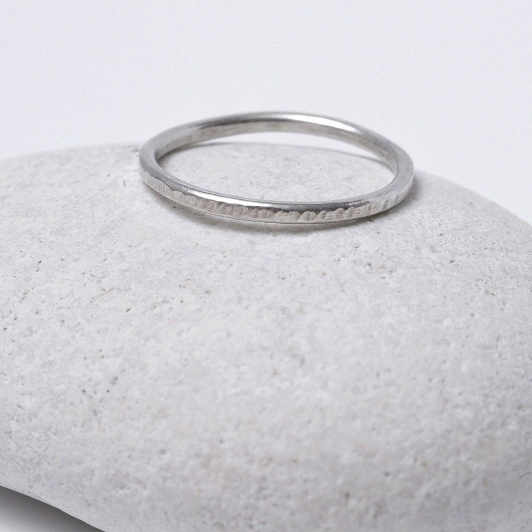 Bague martelée largeur 1.5 mm en argent, présentée sur un galet blanc.