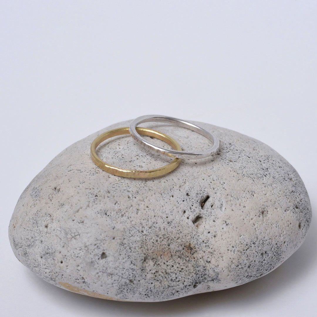 Anneau en or 18 carats et en argent présentés sur un galet fond gris.