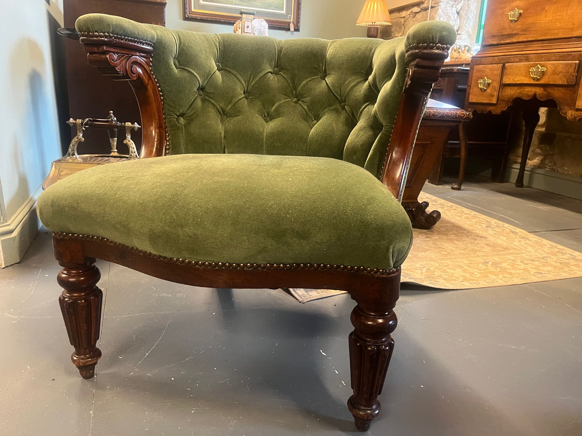 Victorian tub armchair with green upholstery, carved scroll arms and turned front legs