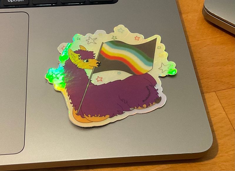 sur un ordinateur portable le sticker de Barbouille le lama violet allongé et tenant dans sa bouche le drapeau handi