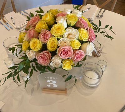 a lovely gold compote wedding centerpiece featuring three dozen fresh roses in shades of yellow, cream and pink