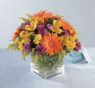 a clear glass cube of yellow and orange flowers for fall, including gerbera daisies and alstromeria