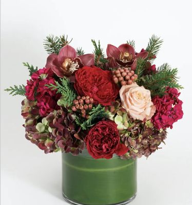 a christmas cylinder vase in festive burgundy and green featuring berries, peonies, roses, orchids, and hydrangeas