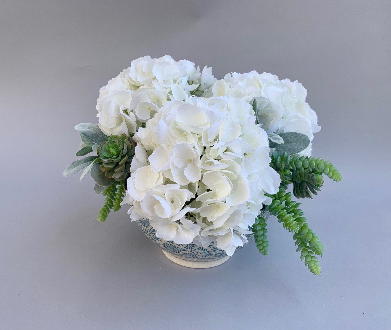 White hydrangeas and dusty succulents in a light blue and white bowl