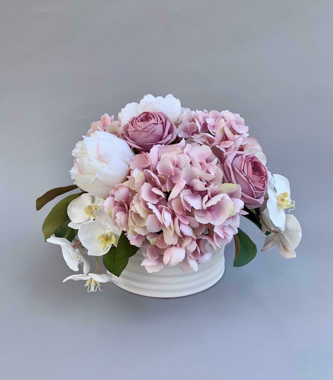 Pink roses and hydrangeas, white peonies and orchids in a white ceramic