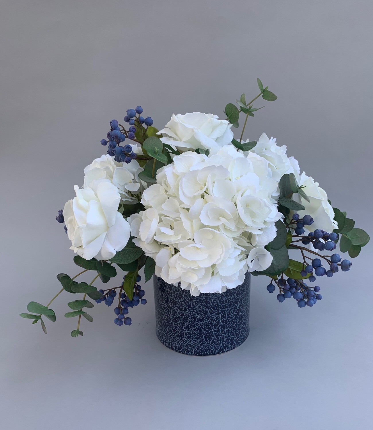 White hydrangeas and roses with blue berries in a denim pot