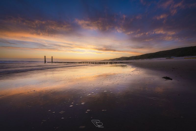 Kleurrijke lucht reflecteert op het strand Valkenisse