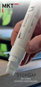 A close-up of a hand applying a white MKT StopGap edge banding sealer pen to the edge of a light wood-grain panel.