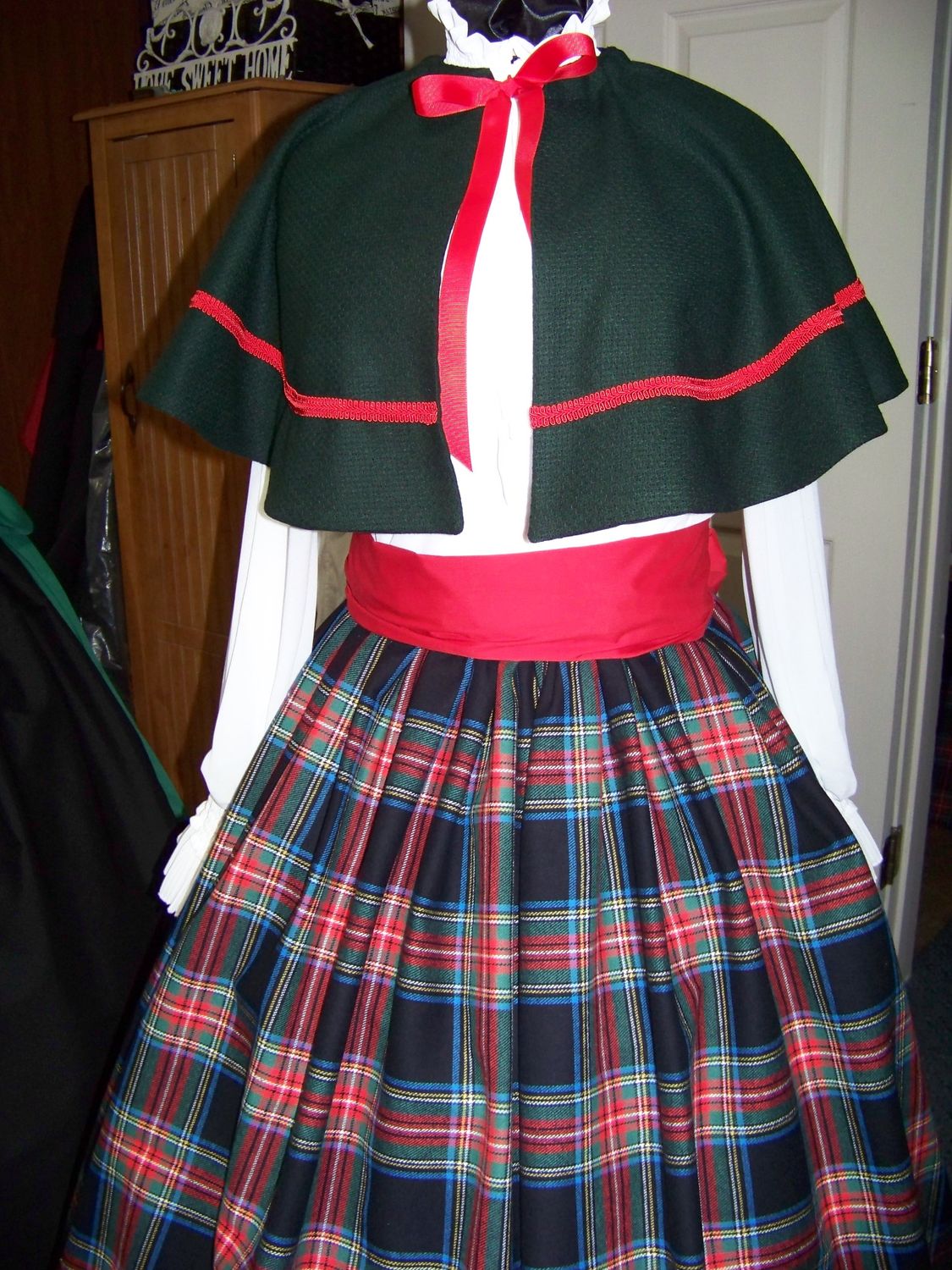 Christmas Caroler cape Hunter green solid wool blend cape reversible one size fits most with black, red, green, blue, white and yellow plaid flannel skirt and red sash. Handmade USA.