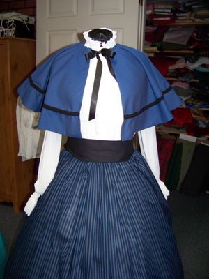 Christmas Caroler cape Williamsburg blue cotton blend cape reversible one size fits most with black and blue stripe cotton blend skirt and black sash. Handmade USA.
