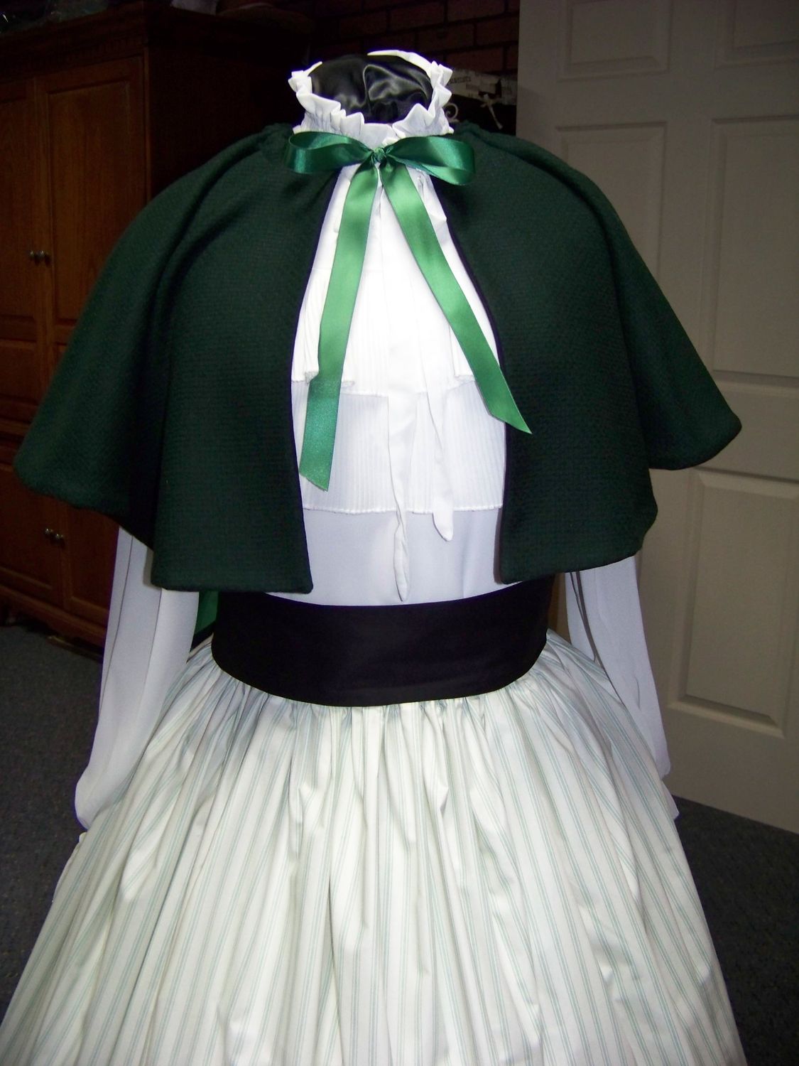 Christmas Caroler cape Hunter green solid wool blend cape reversible with black on inside one size fits most with green and beige stripe skirt cotton with black sash. Handmade USA.