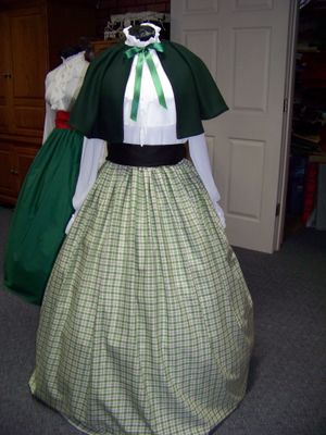 Christmas Caroler cape Hunter green solid wool blend cape reversible with black on inside one size fits most with black, green and beige plaid cotton homespun skirt and black sash. Handmade USA.