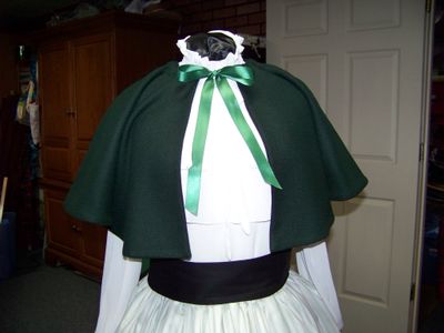 Christmas Caroler cape Hunter green solid wool blend cape reversible with black on inside one size fits most with green and beige stripe skirt cotton with black sash. Handmade USA.