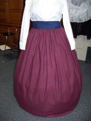 Dicken's Christmas 3-piece outfit Navy-Blue, Cranberry and yellow small checked flannel skirt and cape with solid Navy-blue sash and lining and braid trim.