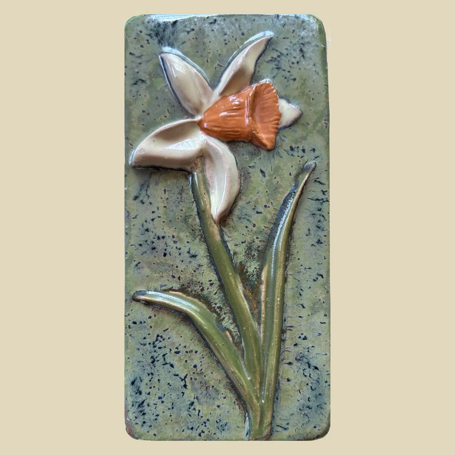 A pretty green tile featuring an orange trumpeted daffodil with pale yellow petals 