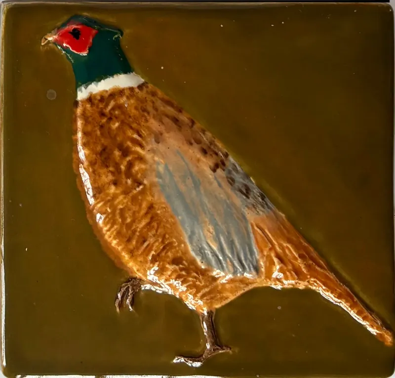 A ceramic feature tile, showing a  pheasant in green,grey and brown set against an olive green background, 1cm x 10.5cm