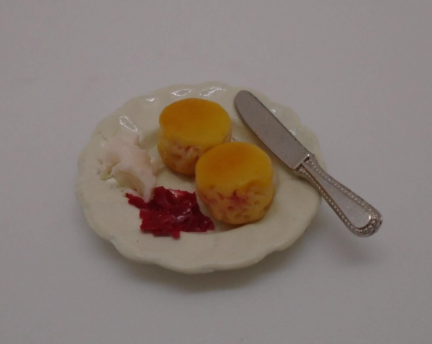 FRUIT SCONES WITH CREAM AND JAM ON CHINA PLATE WITH KNIFE