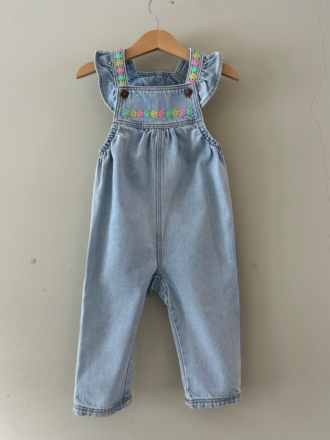 Baby tuinbroekje met bloemetjes randjes en roezel schouderbandjes. Mt 86