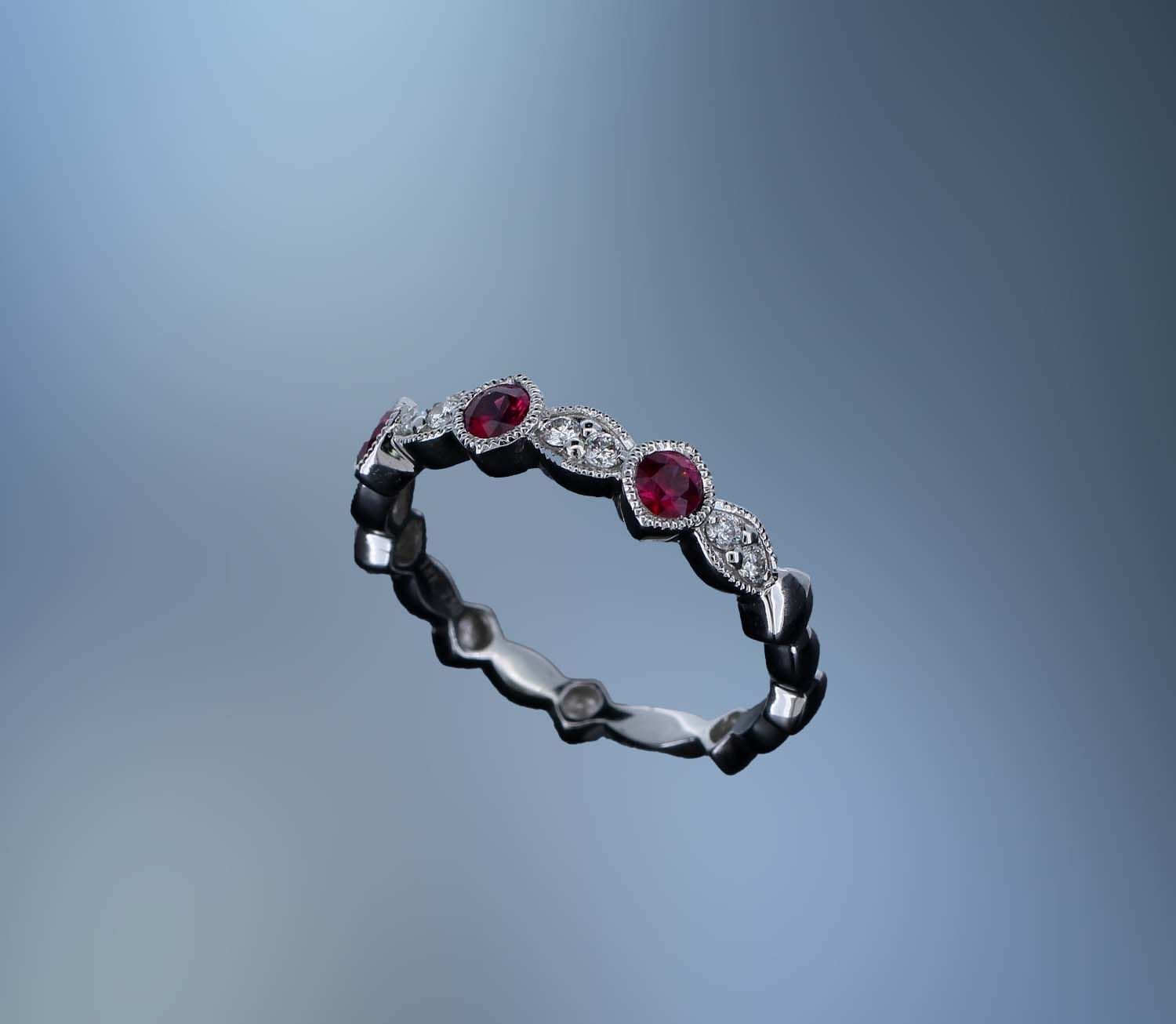 18KT WHITE GOLD DIAMOND & RUBY BAND FEATURING 3 ROUND RUBIES TOTALING .32 CTS & 8 ROUND BRILLIANT DIAMONDS TOTALING .11 CTS 18KT WHITE GOLD DIAMOND & RUBY BAND FEATURING 3 ROUND RUBIES TOTALING .32 CTS & 8 ROUND BRILLIANT DIAMONDS TOTALING .11 CTS