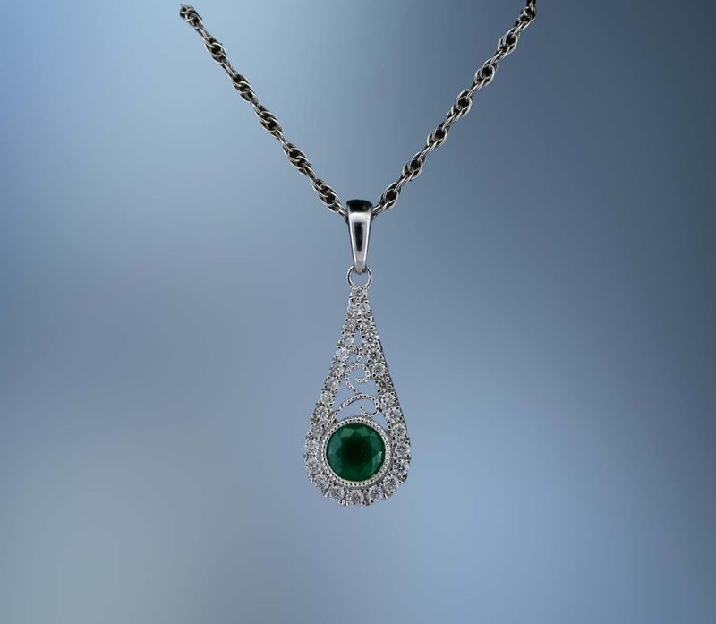 14KT WHITE GOLD LADY'S PENDANT FEATURING ONE ROUND BRILLIANT CUT EMERALD TOTALING .30 CTS AND 28 ROUND BRILLIANT CUT  DIAMOND TOTALING .12 CTS