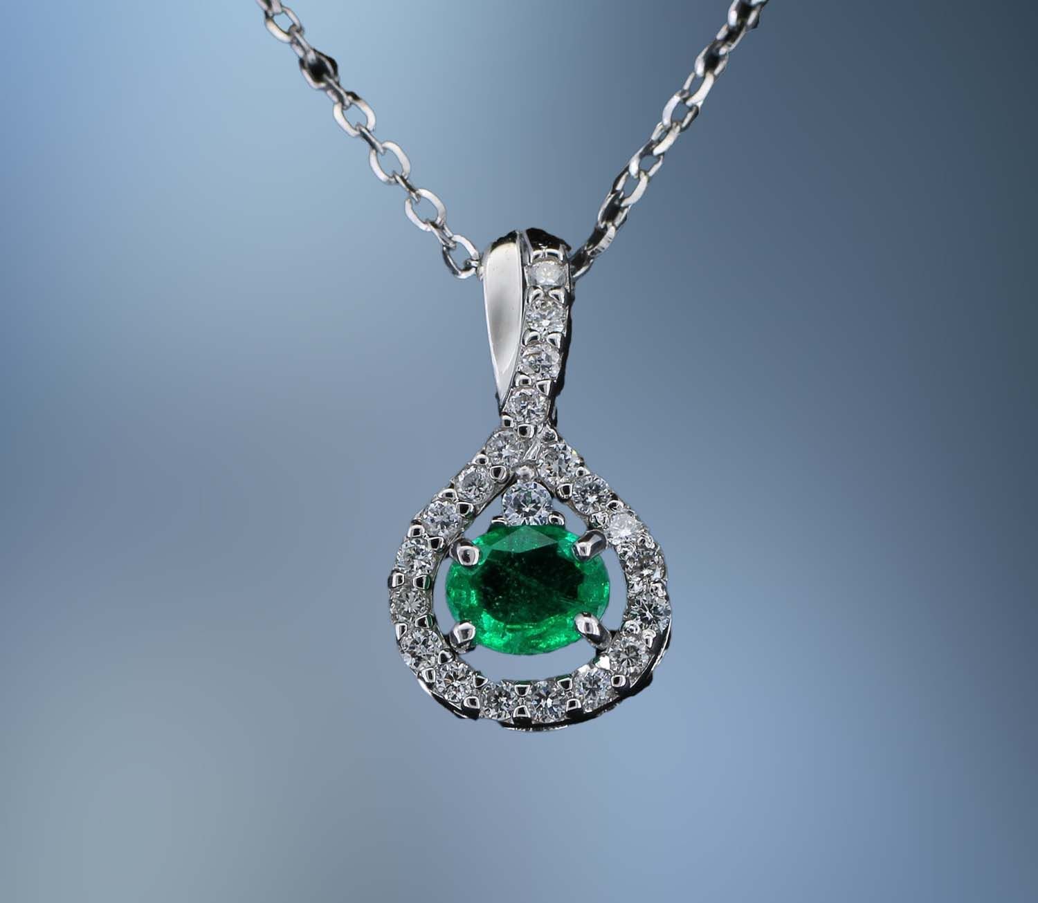 18 KT WHITE GOLD DIAMOND AND EMERALD PENDANT FEATURING 1 OVAL NATURAL EMERALD TOTALING 0.58 CTS AND 21 ROUND BRILLIANT CUT DIAMONDS TOTALING 0.26 CTS 18 KT WHITE GOLD DIAMOND AND EMERALD PENDANT FEATURING 1 OVAL NATURAL EMERALD TOTALING 0.58 CTS AND 21 ROUND BRILLIANT CUT DIAMONDS TOTALING 0.26 CTS