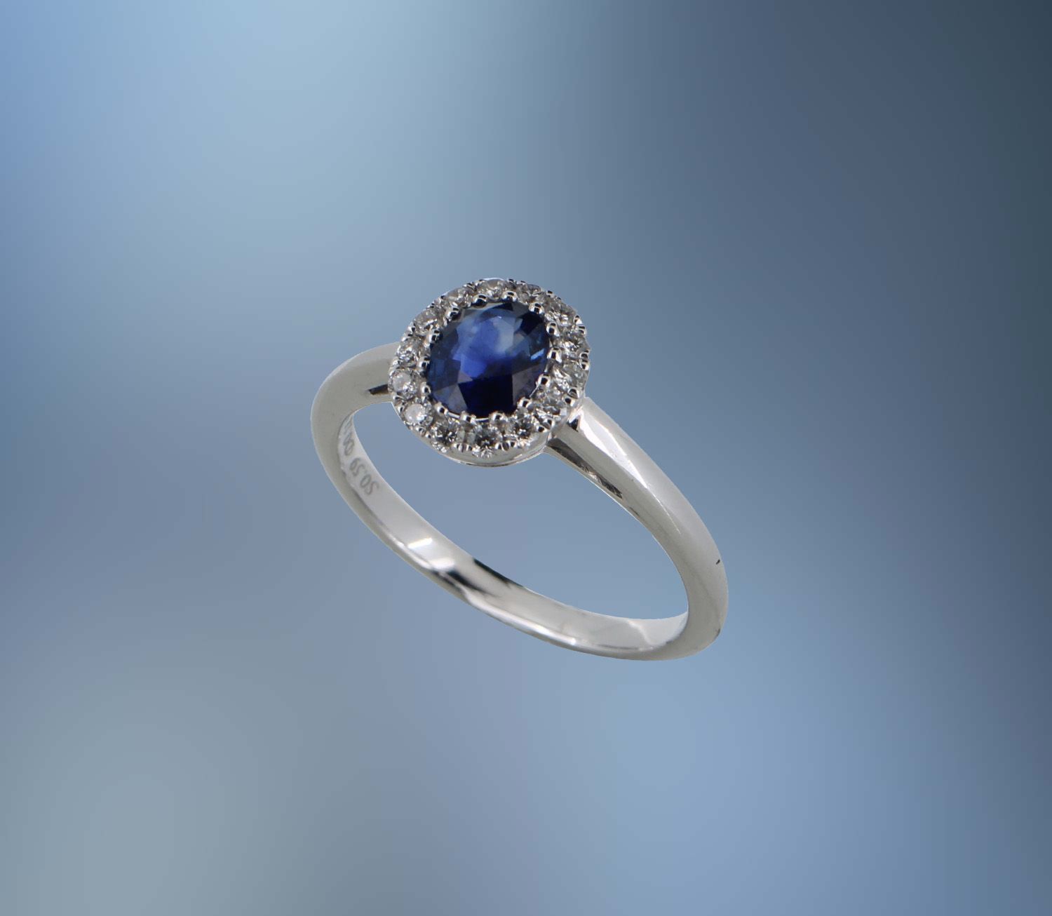 18KT WHITE GOLD DIAMOND & SAPPHIRE HALO STYLE RING FEATURING ONE OVAL SAPPHIRE TOTALING 0.59 CTS AND   14 ROUND BRILLIANT CUT DIAMONDS TOTALING .18 CTS