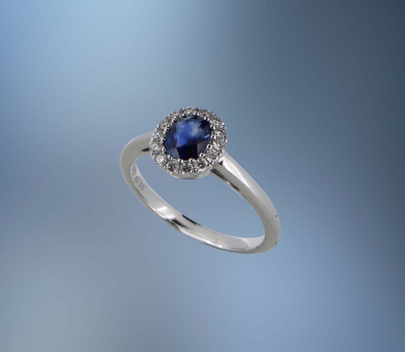 18KT WHITE GOLD DIAMOND & SAPPHIRE HALO STYLE RING FEATURING ONE OVAL SAPPHIRE TOTALING 0.59 CTS AND   14 ROUND BRILLIANT CUT DIAMONDS TOTALING .18 CTS
