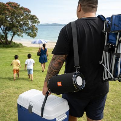 Man carrying portable Bluetooth speaker and cooler walking toward beach with family