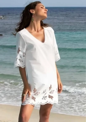 Lise Charmel Envolee Tropicale White Tunic. The dress has refined detailing and cut work embroidery to the sleeves and hemline. Pictured by the sea.