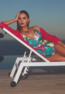 Frida Swimsuit by Nuria Ferrer. The fabric is a colourful marbled effect print. The suit is fully lined with a figure shaping mesh and a tummy smoother to the front. A gentle v-neckline is combined with soft foam lined cups. The shoulder straps are ornamented with pink metal loops and are adjustable to give a comfortable fit. Lifestyle photo.